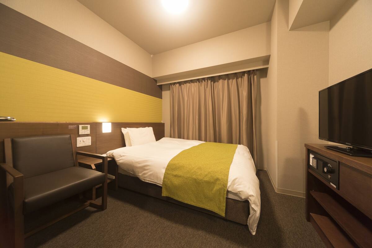 A hotel room with a bed, a TV, a desk, and a chair.