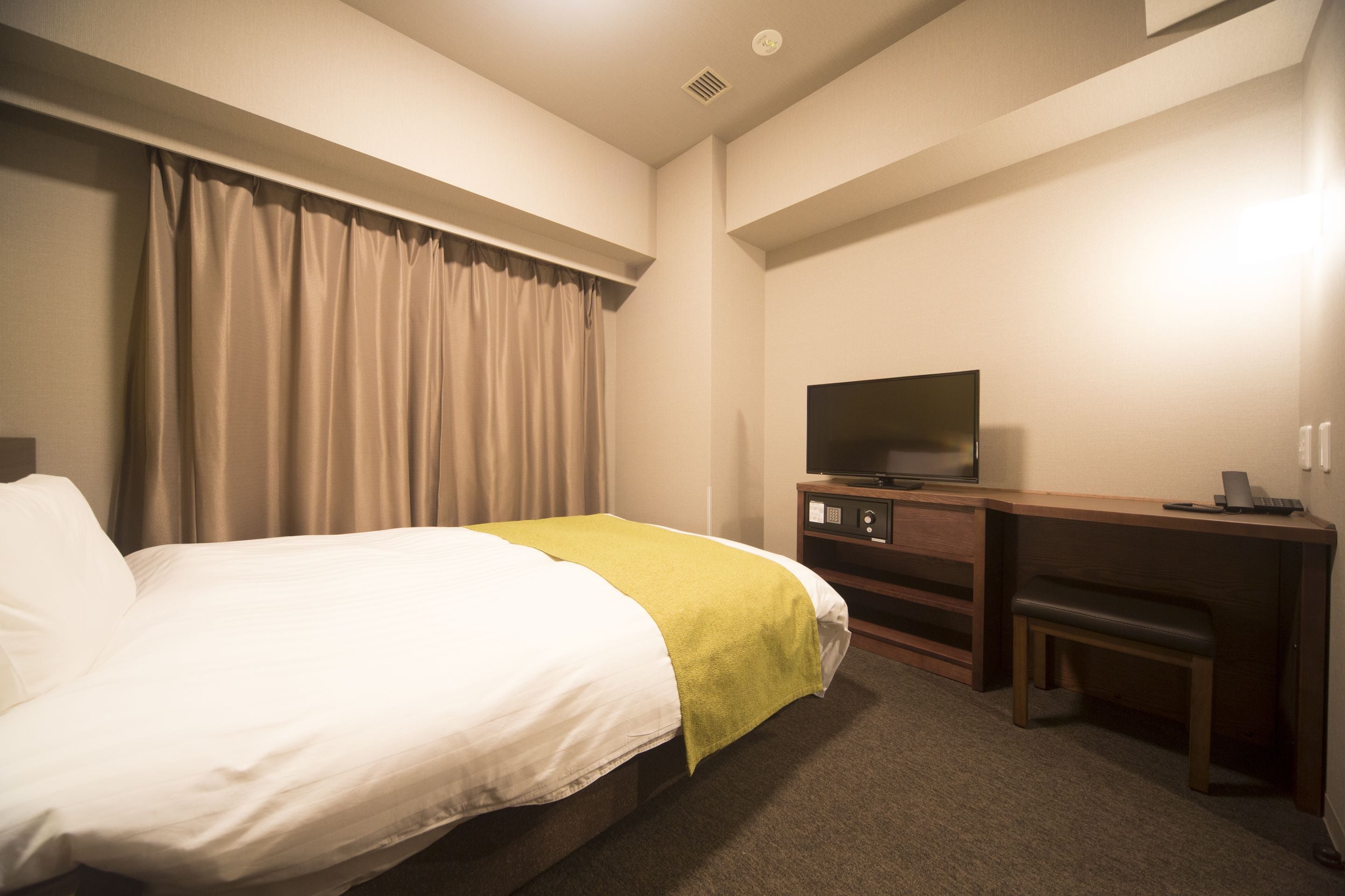 Habitación de hotel con cama, escritorio, silla, televisor y ventana con cortinas.