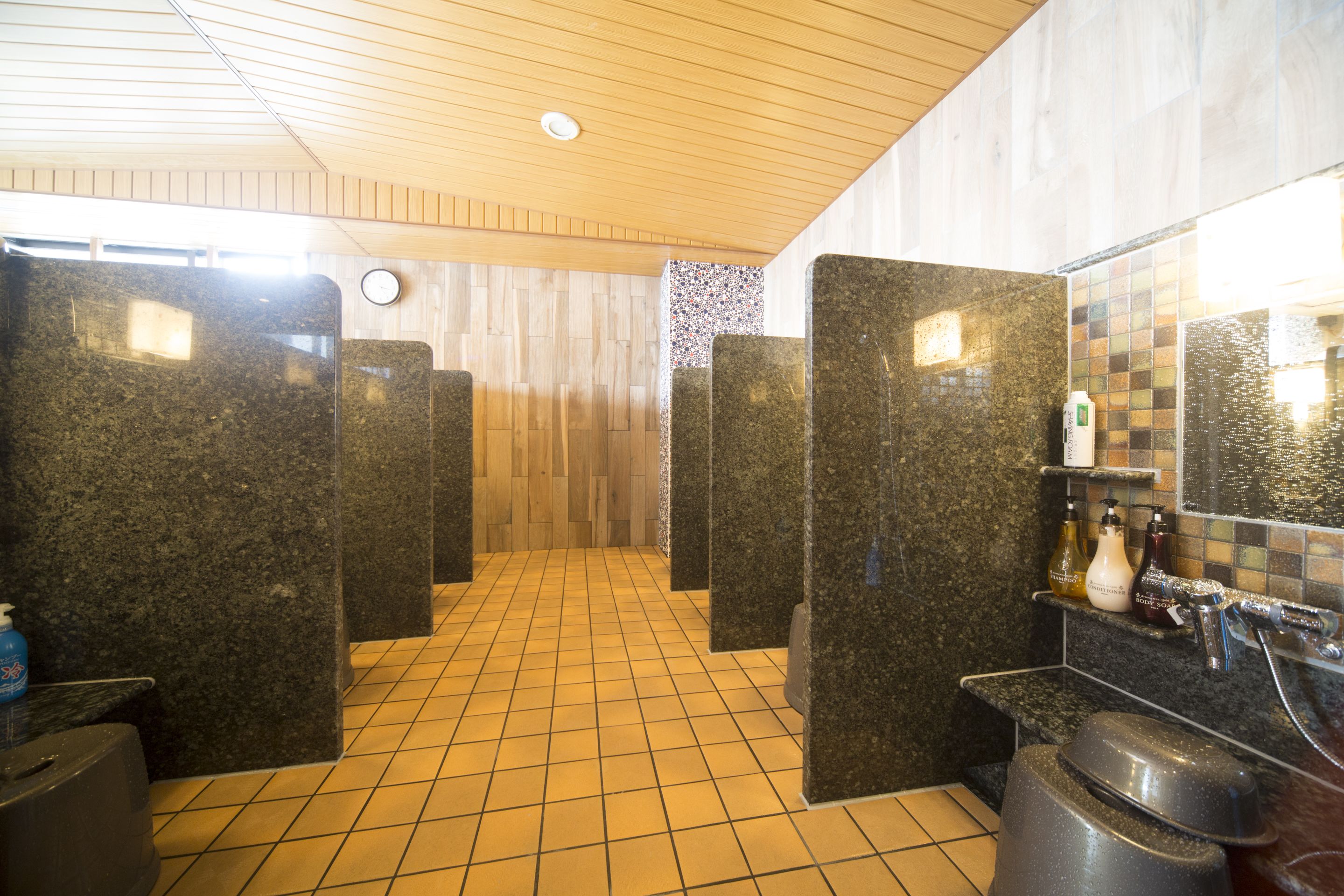 A public restroom with granite counters, a tiled floor, and a wooden ceiling.