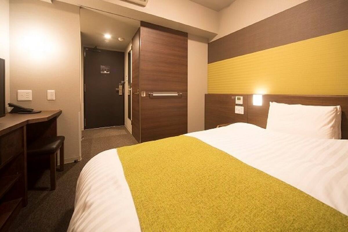 A hotel room with a bed, a desk, and a door leading to a bathroom.