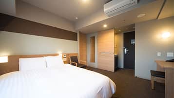 A hotel room with a large bed, a desk, a chair, and an air conditioning unit.