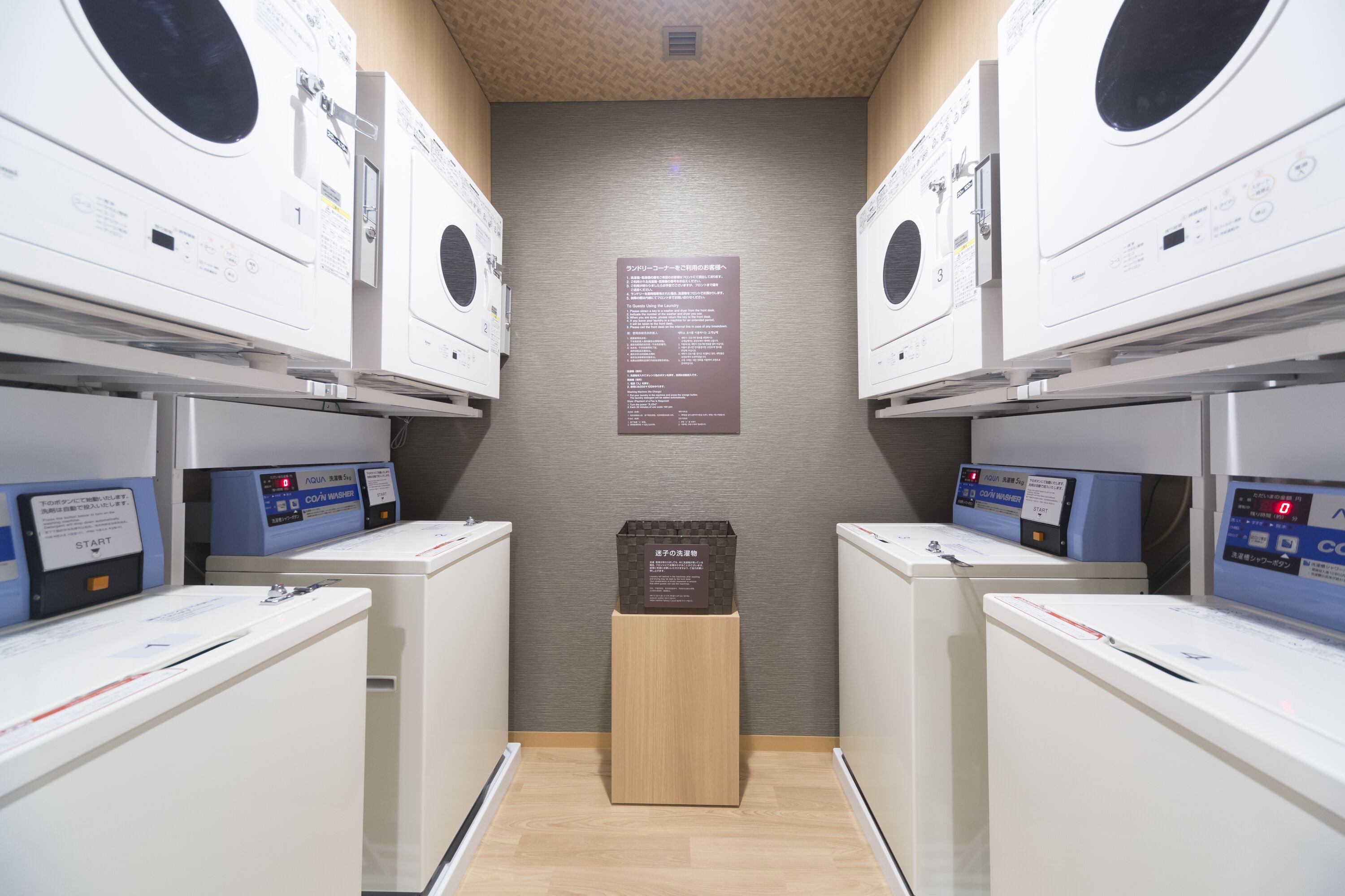 A laundry facility with multiple washing machines and dryers, a wooden floor, and a sign with instructions.