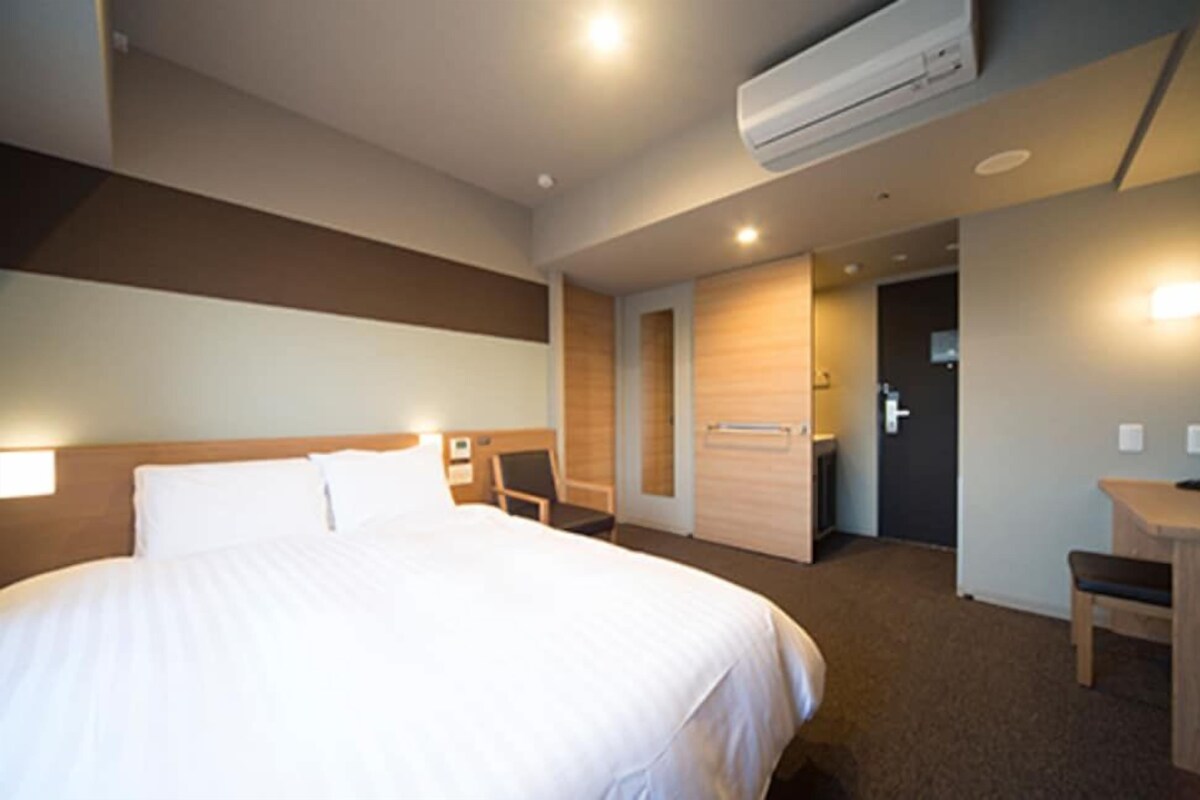Habitación de hotel con cama, escritorio, silla, equipo de aire acondicionado y puerta que da a un baño.