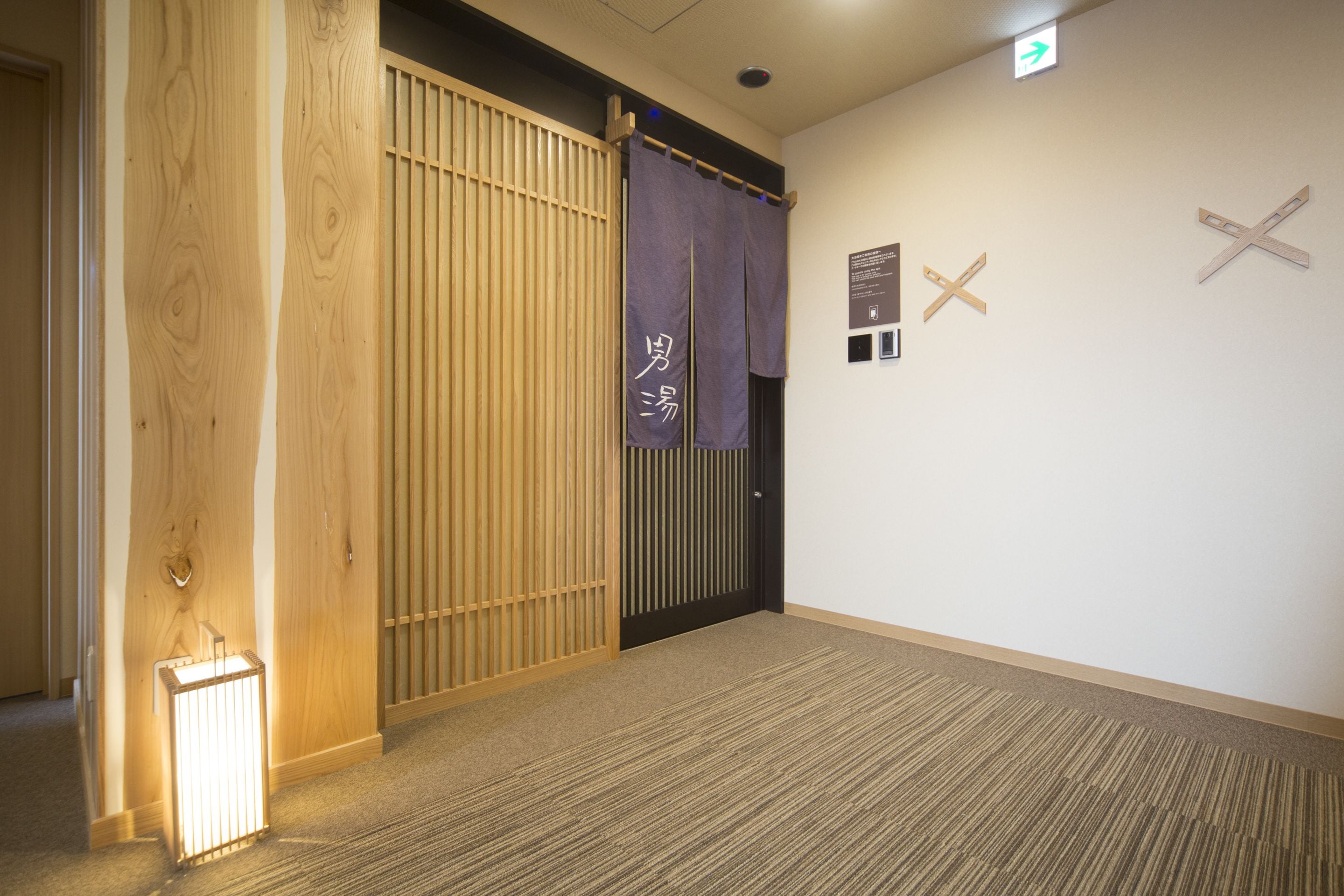 Un pasillo con una puerta de madera, una lámpara de pie iluminada y un cartel con caracteres japoneses.