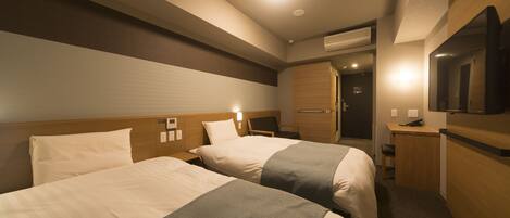 A hotel room with two beds, a desk, a chair, a TV, and an air conditioning unit.