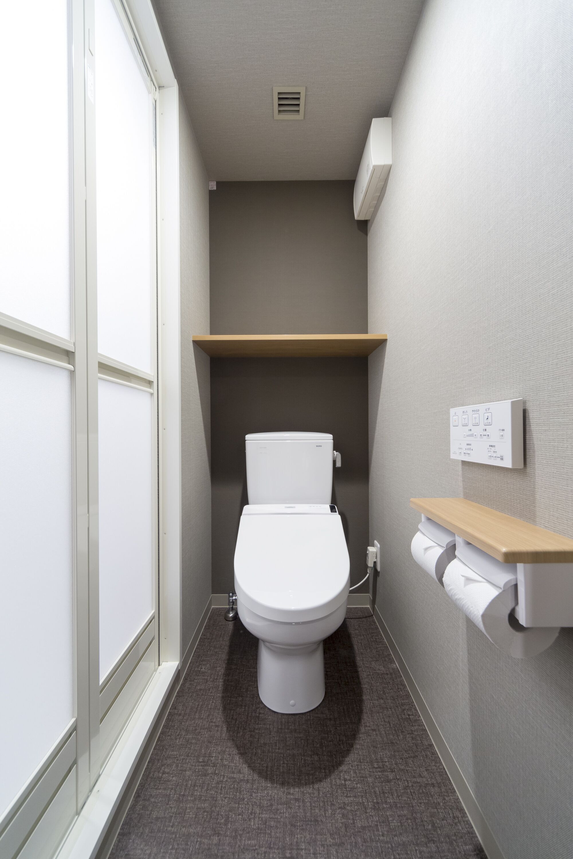 Un baño pequeño con inodoro, dispensador de toallas y estante.