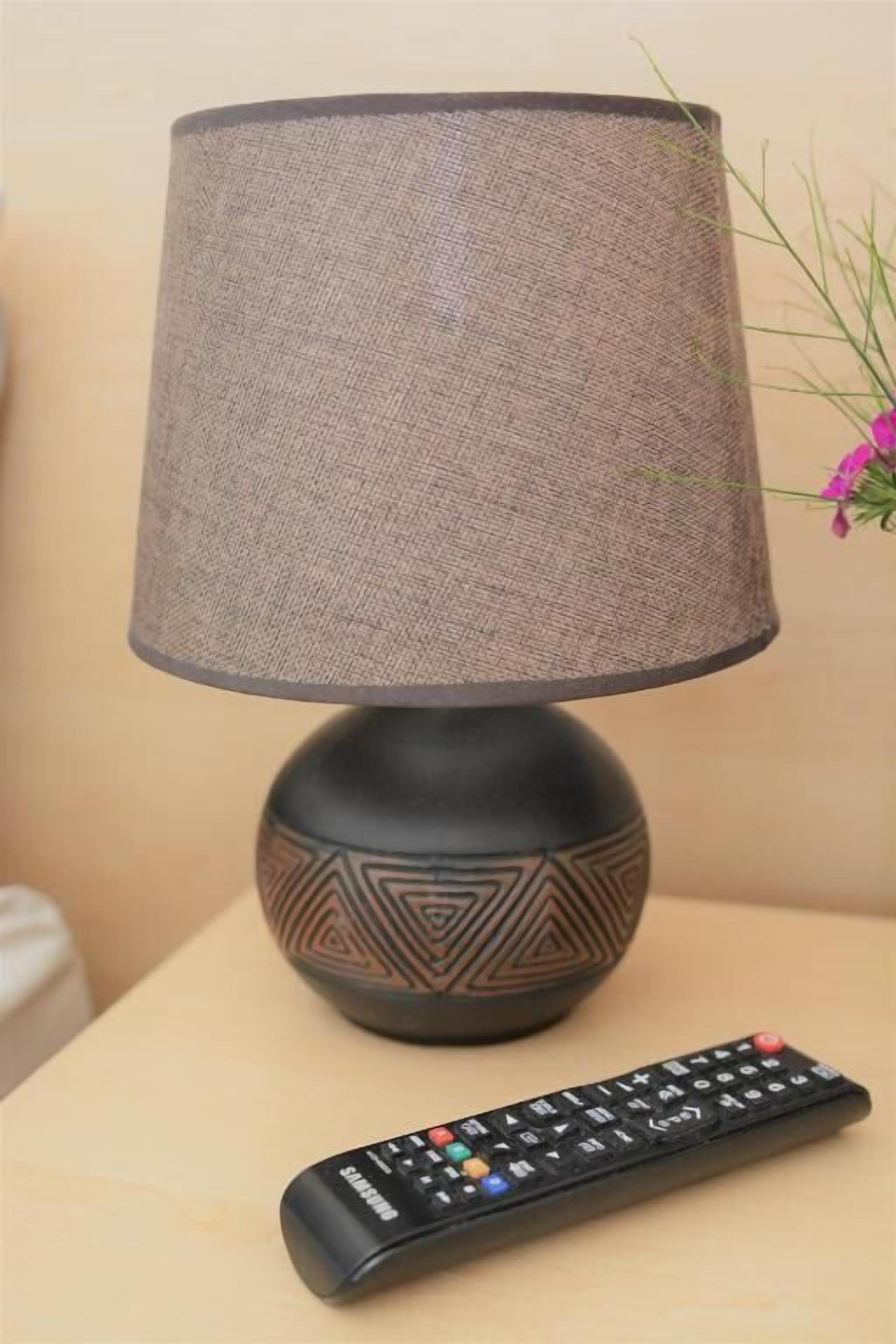 A lamp with a textured lampshade and a remote control on a table.