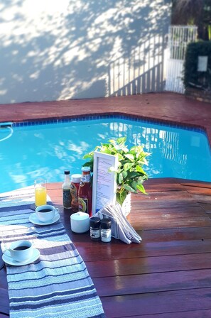 Ein Poolbereich mit Holzterrasse, gestreiftem Handtuch, Speisekarte sowie verschiedenen Gewürzen und Getränken.