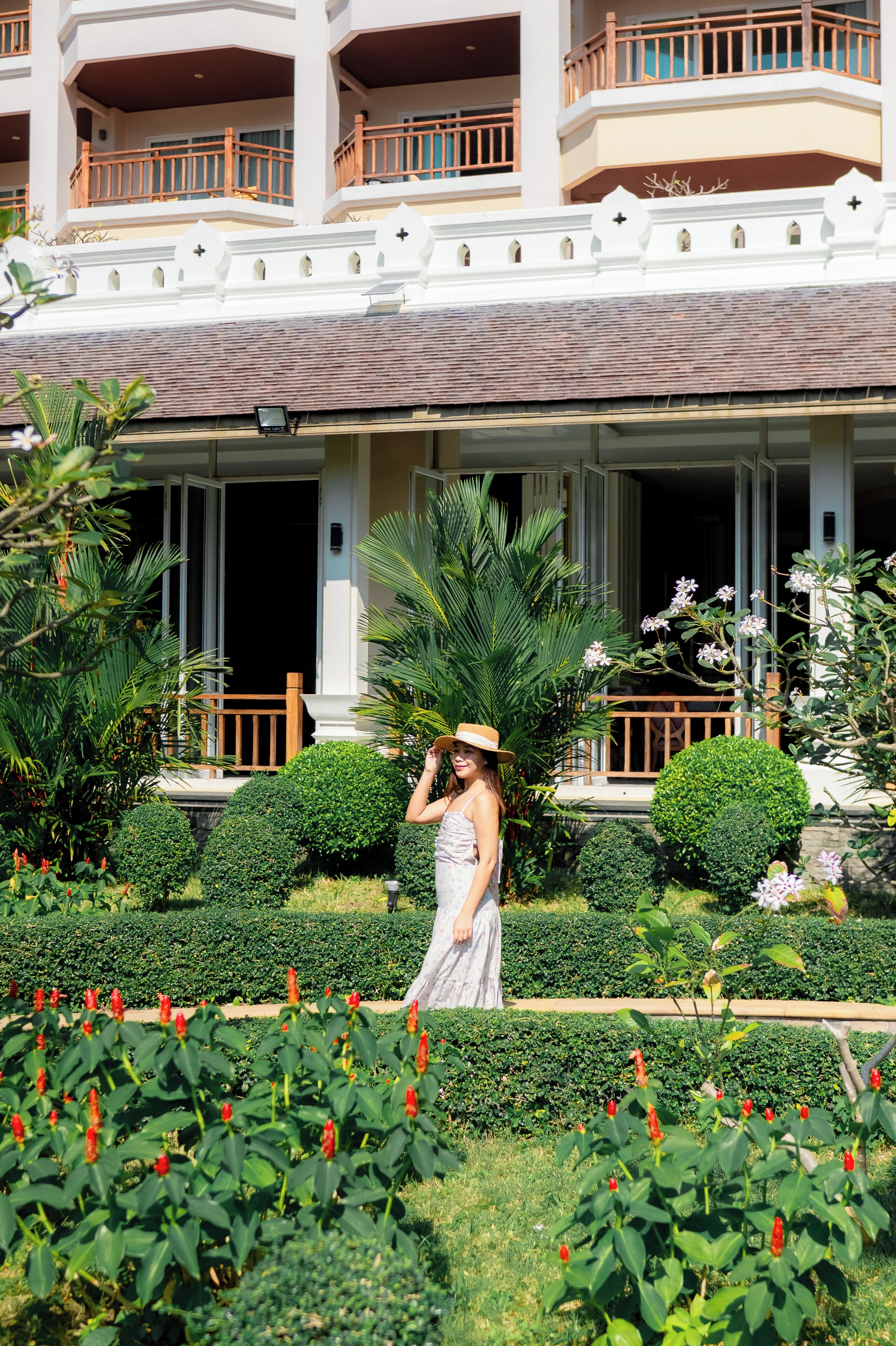 A hotel with a covered outdoor area, a well-maintained garden, and a balcony with wooden railings.