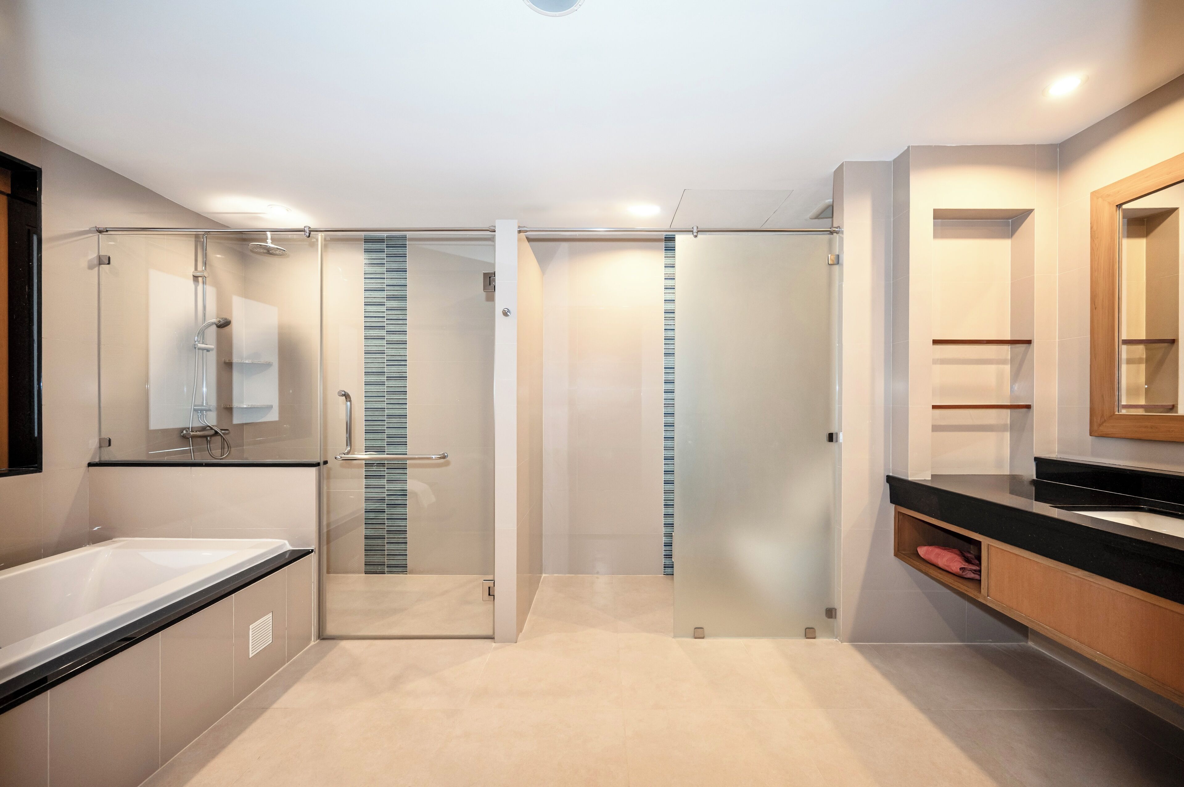 A modern bathroom with a glass-enclosed shower, a large bathtub, and a wooden vanity with a mirror.