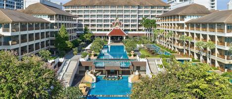A hotel with a central pool, multiple balconies, and surrounding greenery.