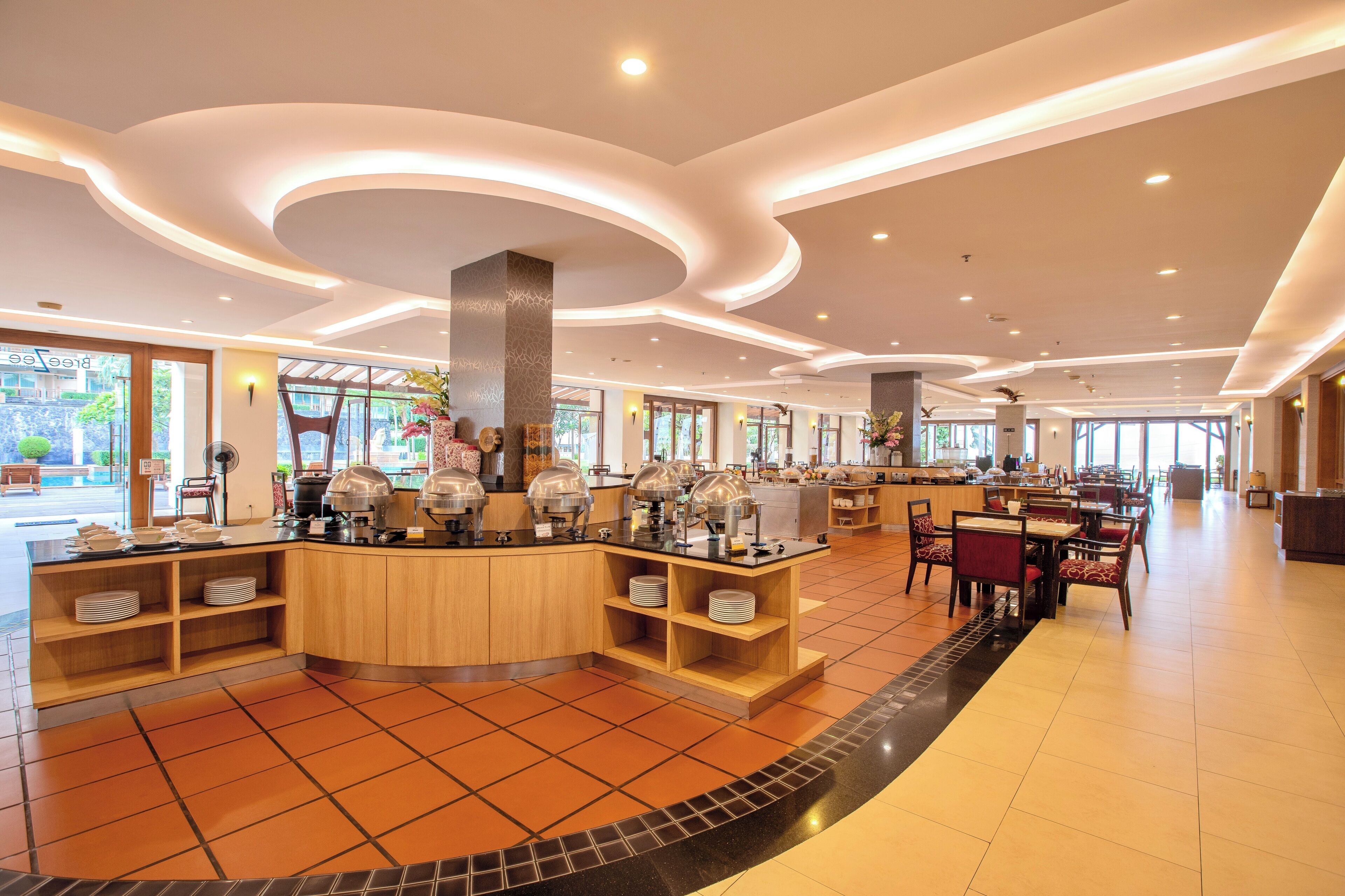 Un hall d’hôtel spacieux doté d’un buffet central, de plusieurs espaces aménagés pour s’asseoir et de grandes fenêtres laissant entrer la lumière naturelle.