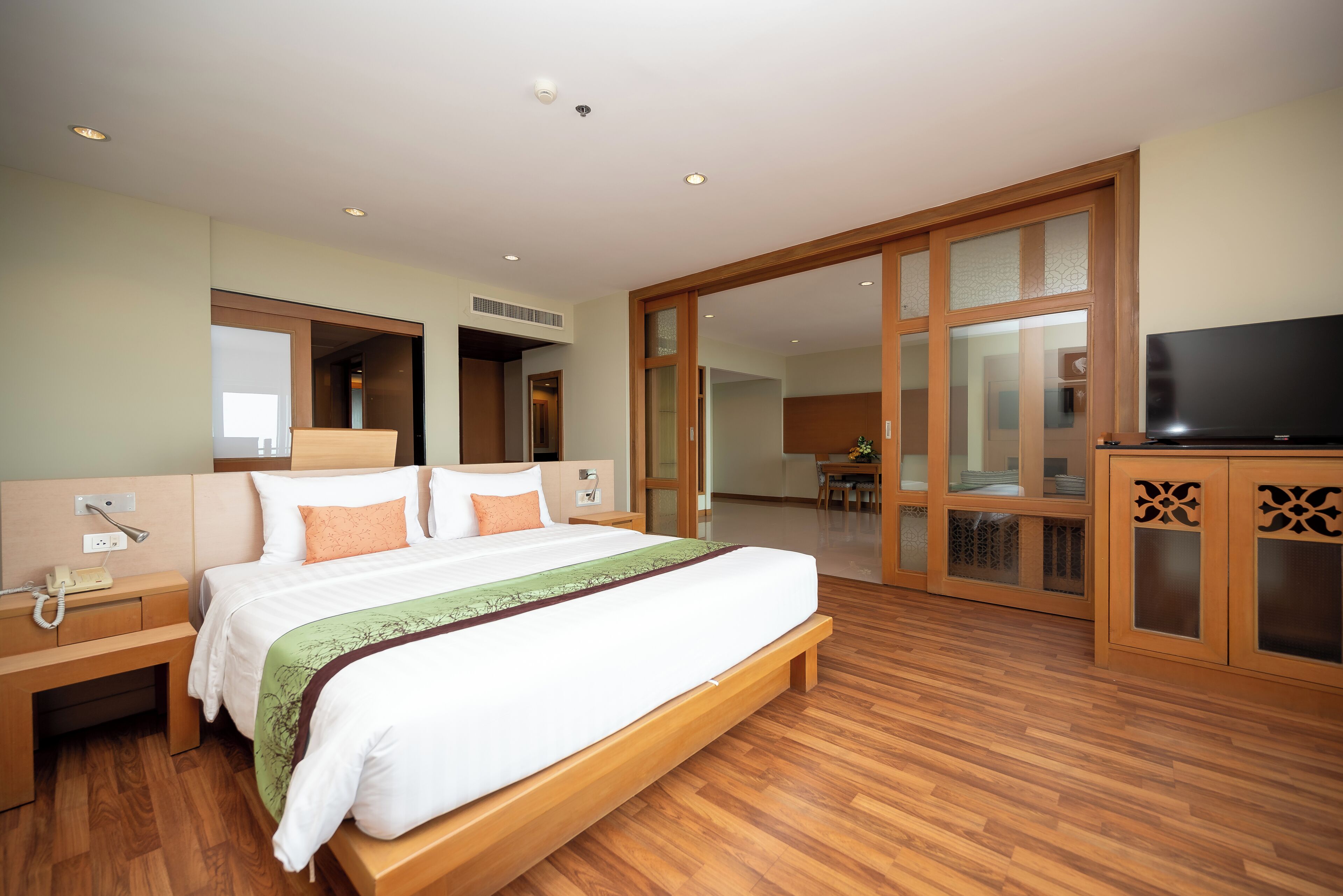 A hotel room with a large bed, wooden flooring, a TV, and a sliding door leading to a dining area.