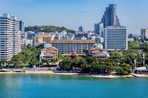 Un paysage urbain côtier avec un hôtel imposant doté d’une cour centrale, entouré de gratte-ciel et bordé d’une plage.