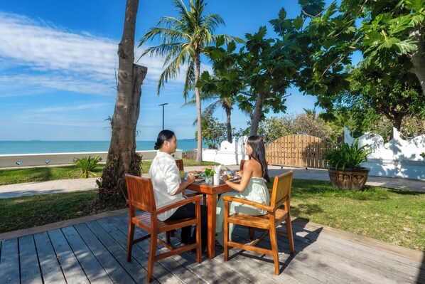 Dos personas cenando en una mesa de madera con vistas a la playa y al océano.