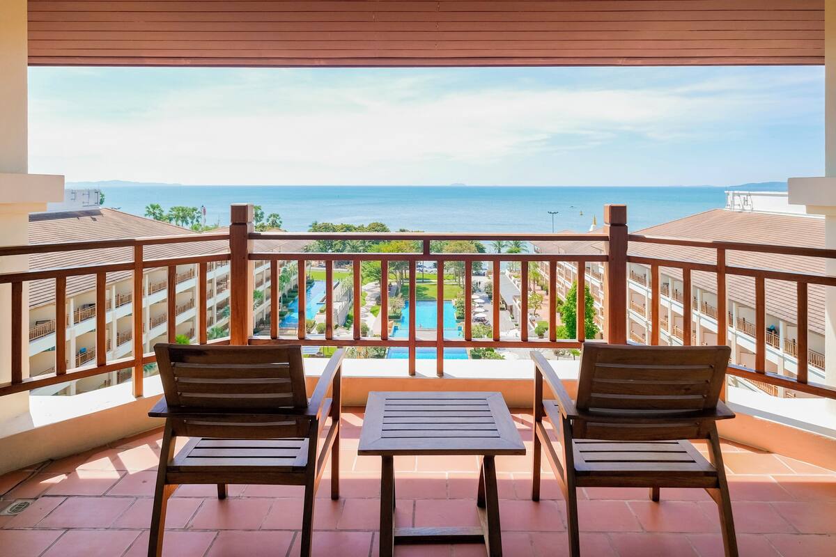 Un balcon doté de mobilier en bois et offrant une vue sur la mer et la piscine.