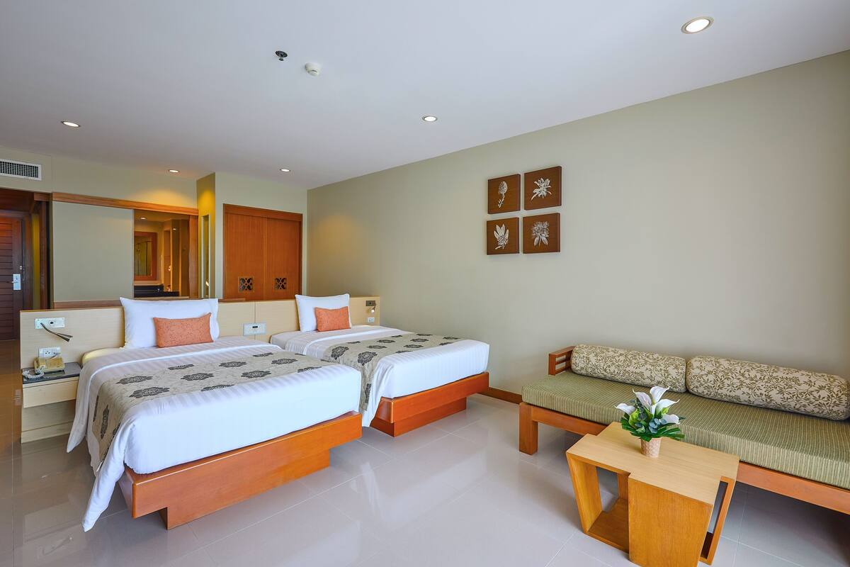 Une chambre d’hôtel avec deux lits, un canapé, une petite table et un mur orné de quatre tableaux encadrés.