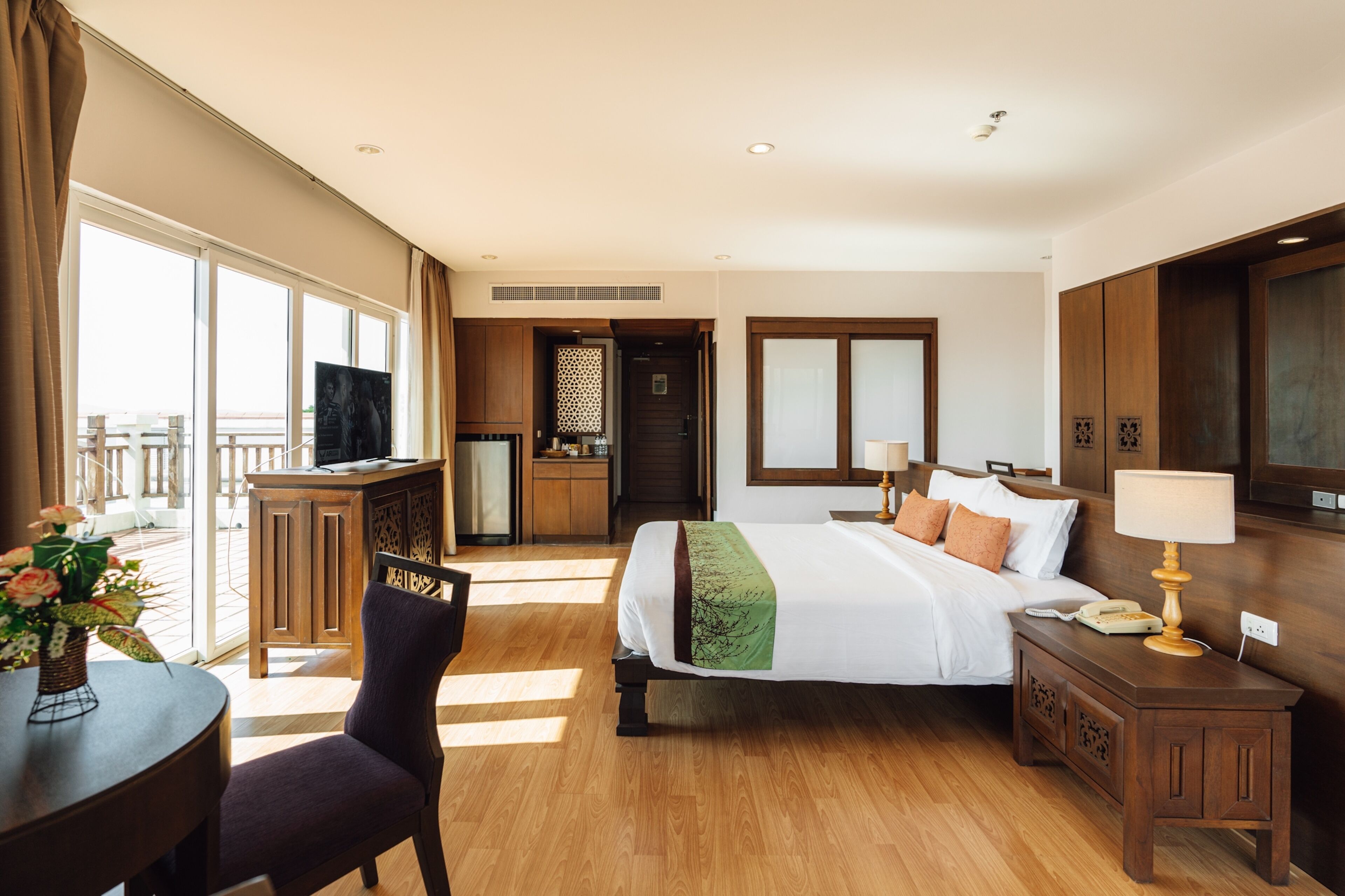 Habitación de hotel con cama, mesitas de noche, escritorio, silla, televisor y balcón con vistas.