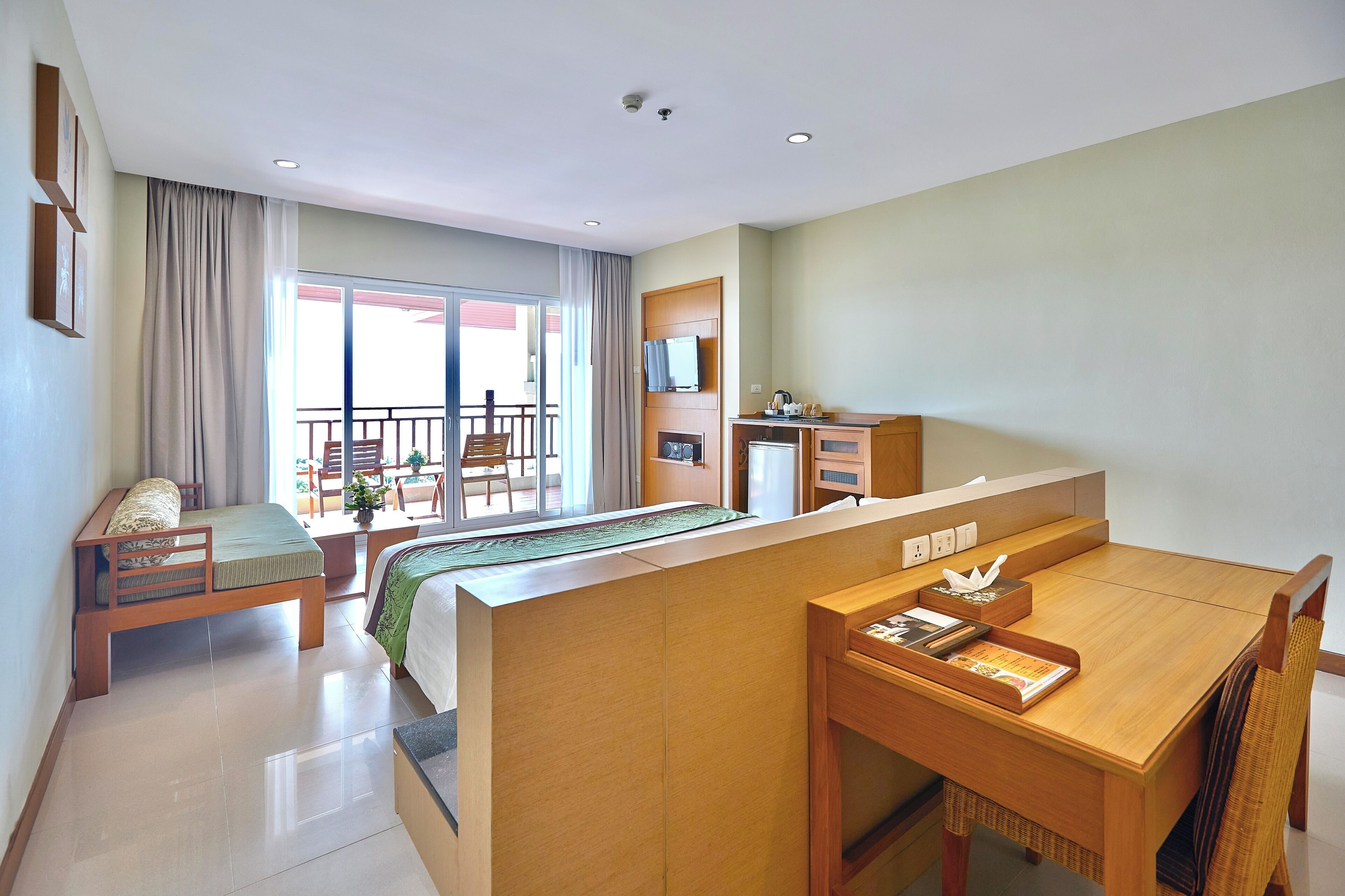 A hotel room with a bed, a desk, a chair, a small table, a TV, and a balcony with a view.