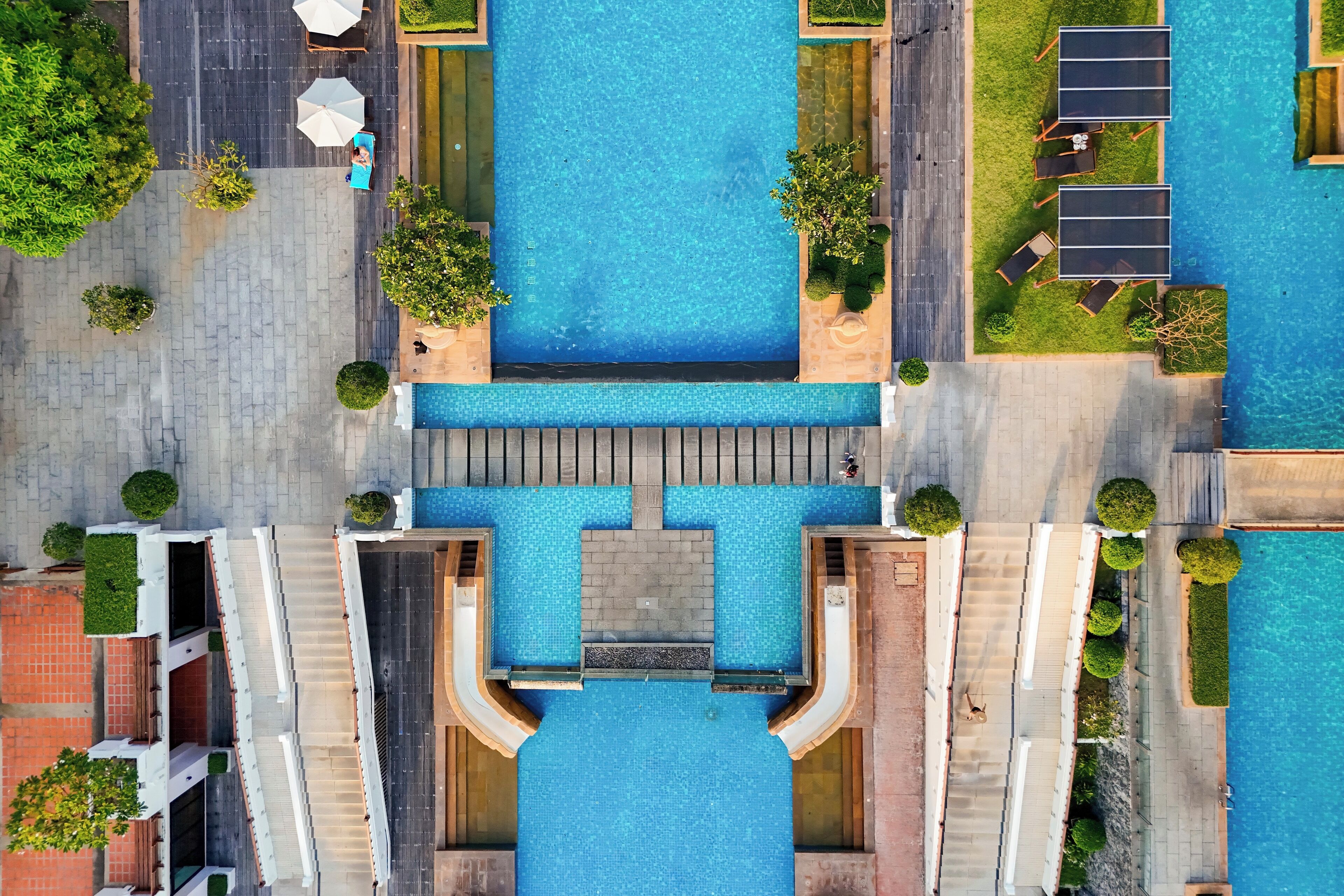 An aerial view of a hotel with a central swimming pool, surrounded by pathways and greenery.