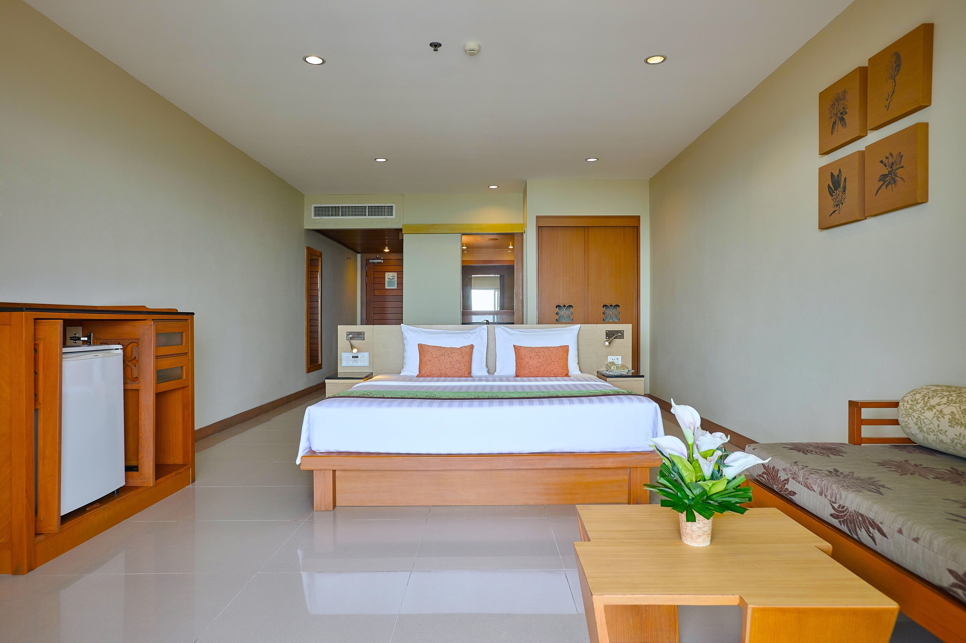 A hotel room with a bed, a small kitchenette, a bedside table with a plant, and a sofa.