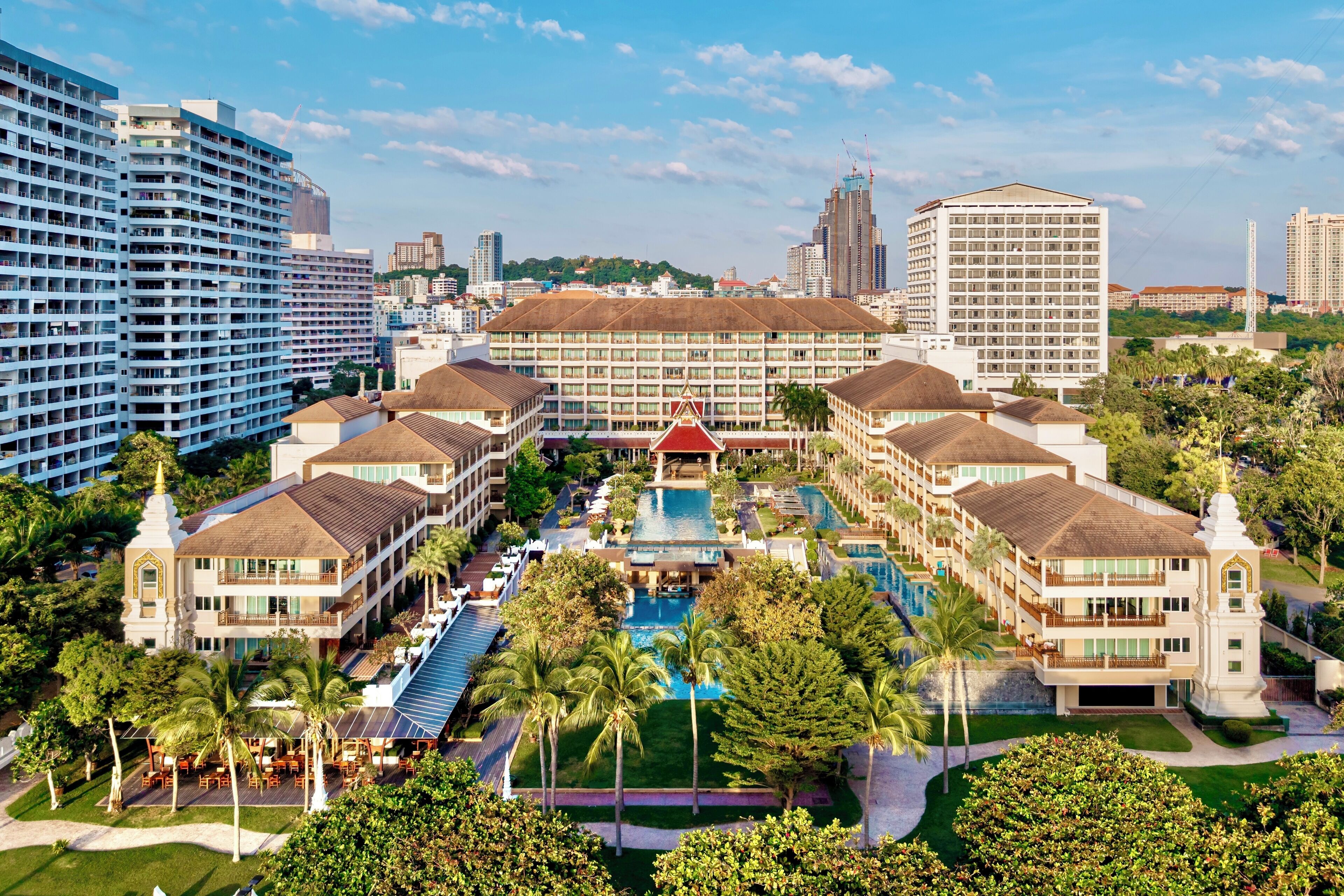 A hotel with multiple buildings, a central pool, and surrounding greenery.