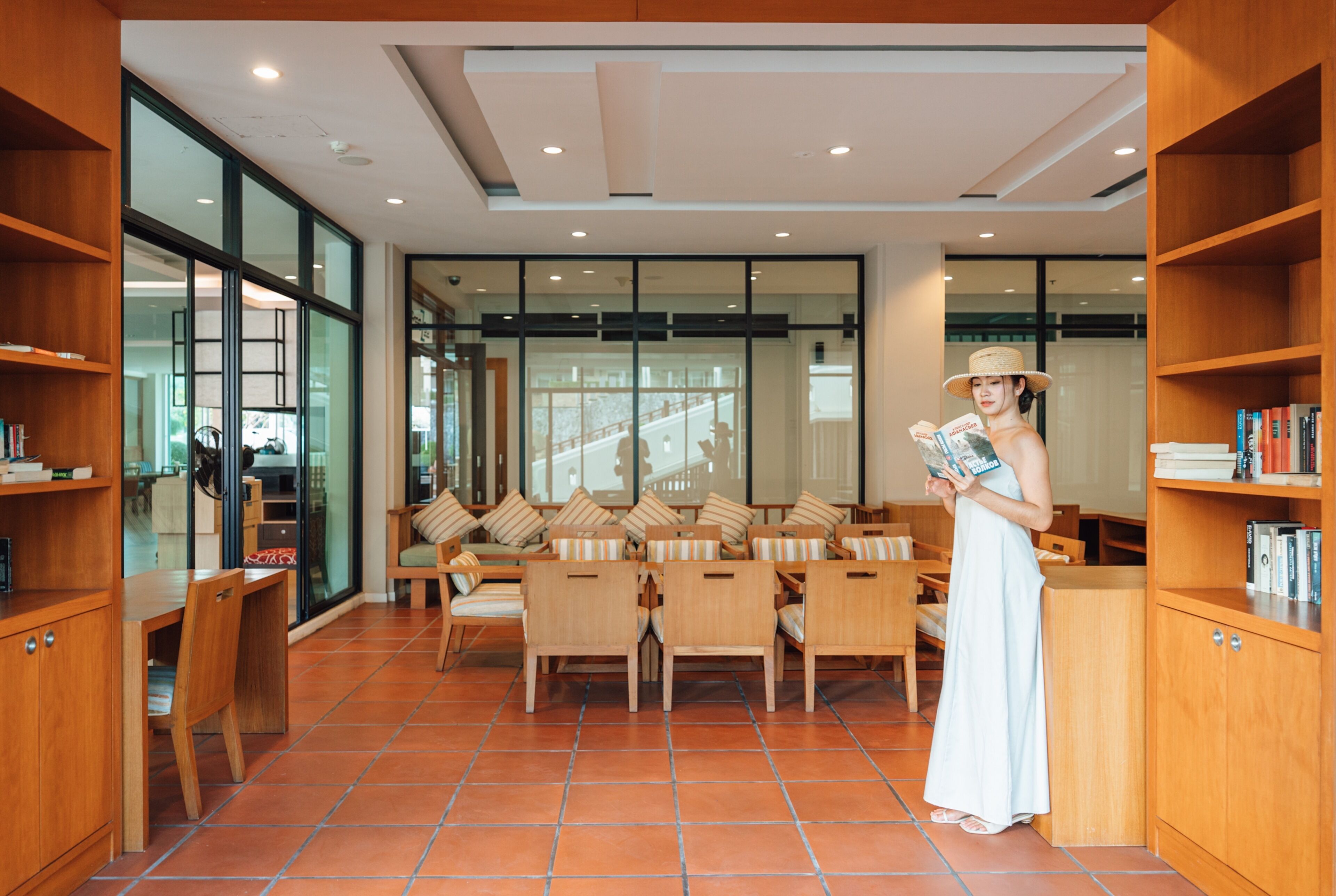 A spacious reading area with wooden furniture, large windows, and bookshelves.