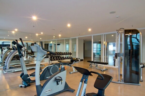 A gym with cardio machines, dumbbells, and a weightlifting area.