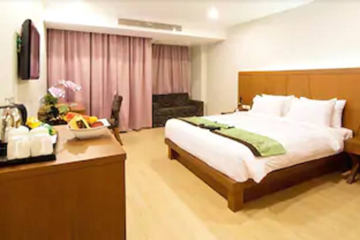 A hotel room with a bed, bedside table, and a desk with a fruit basket.