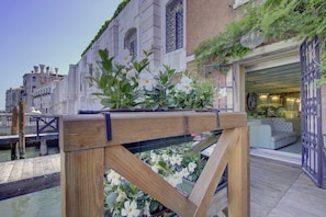 A wooden deck with a railing, a canal, and a building with a blue and white facade. - GranDELUX-Canal (Venice)