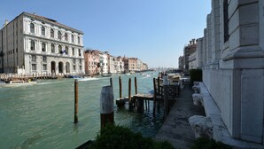 A canal with boats, historic buildings, and a wooden dock with chairs. - GranDELUX-Canal (Venice)