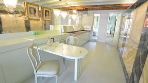 A modern kitchen with white cabinetry, a dining table, and chairs. There are two chandeliers hanging above the table. - GranDELUX-Canal (Venice)