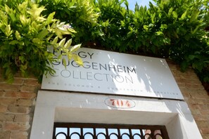 A sign for the Solomon R. Guggenheim Collection, featuring a brick wall and greenery. - GranDELUX-Canal (Venice)