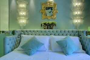A bed with a tufted headboard, two light blue pillows, and a vase with green plants. - GranDELUX-Canal (Venice)