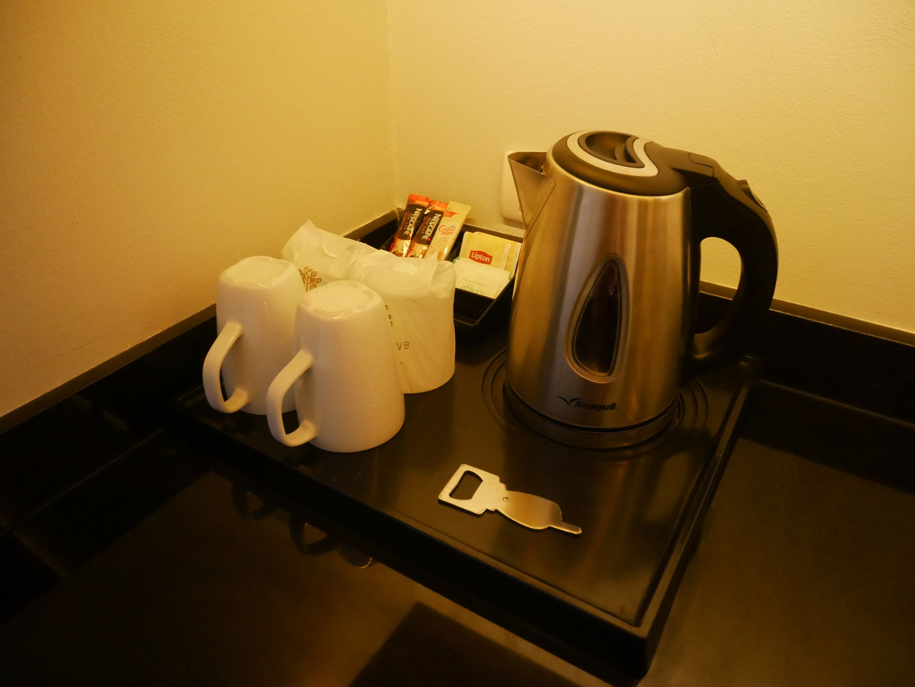 Un plateau avec une bouilloire, trois tasses blanches et une boîte de sachets de thé Lipton.
