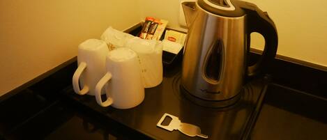 Un plateau avec une bouilloire, trois tasses blanches et une boîte de sachets de thé Lipton.