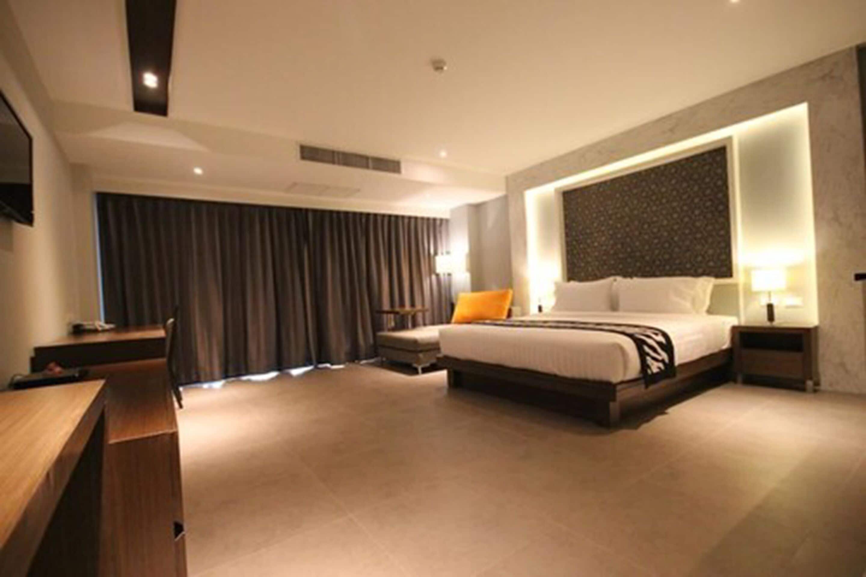 A modern hotel room with a large bed, a desk, and a seating area.