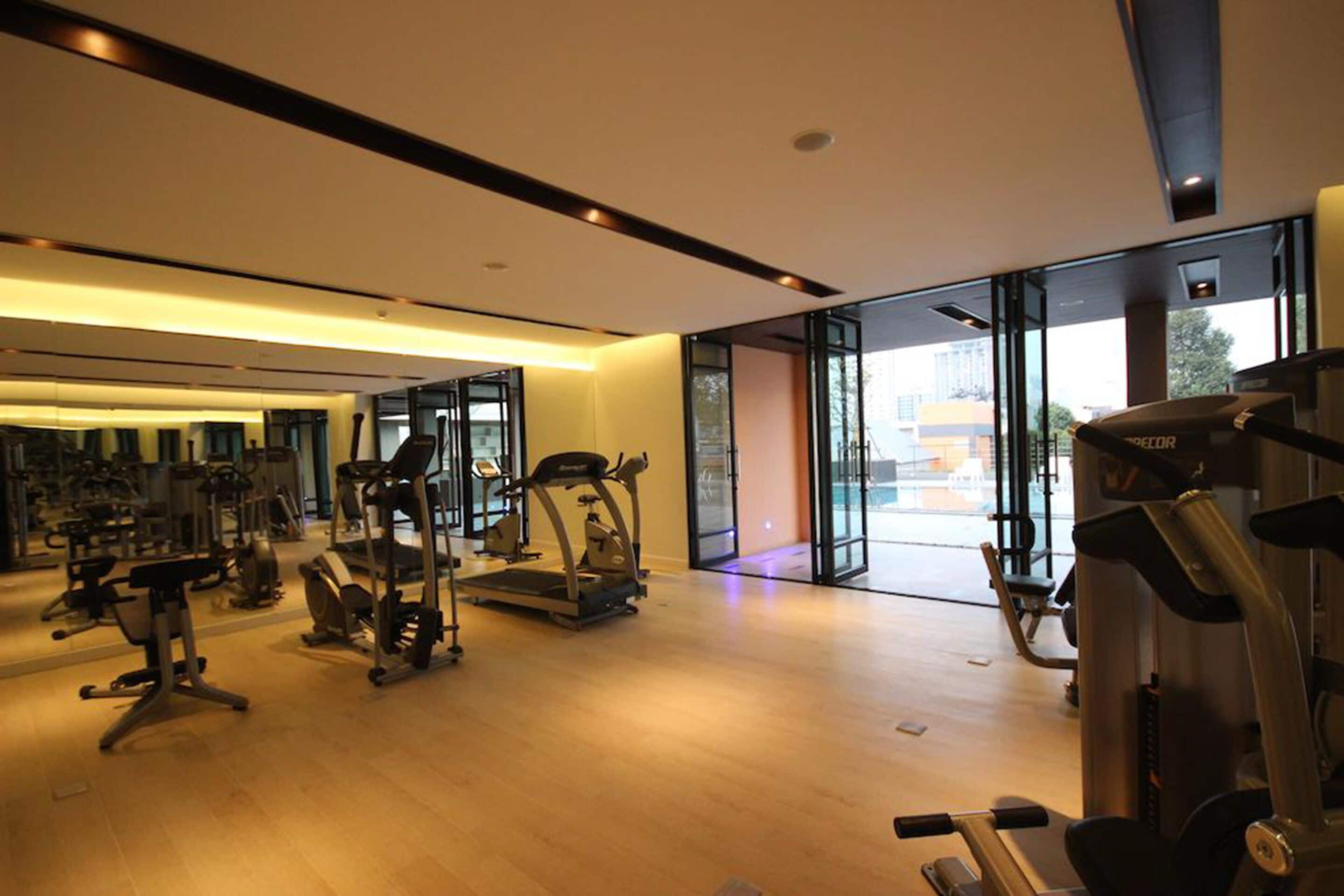 A modern gym with various exercise equipment, large windows, and a spacious layout.