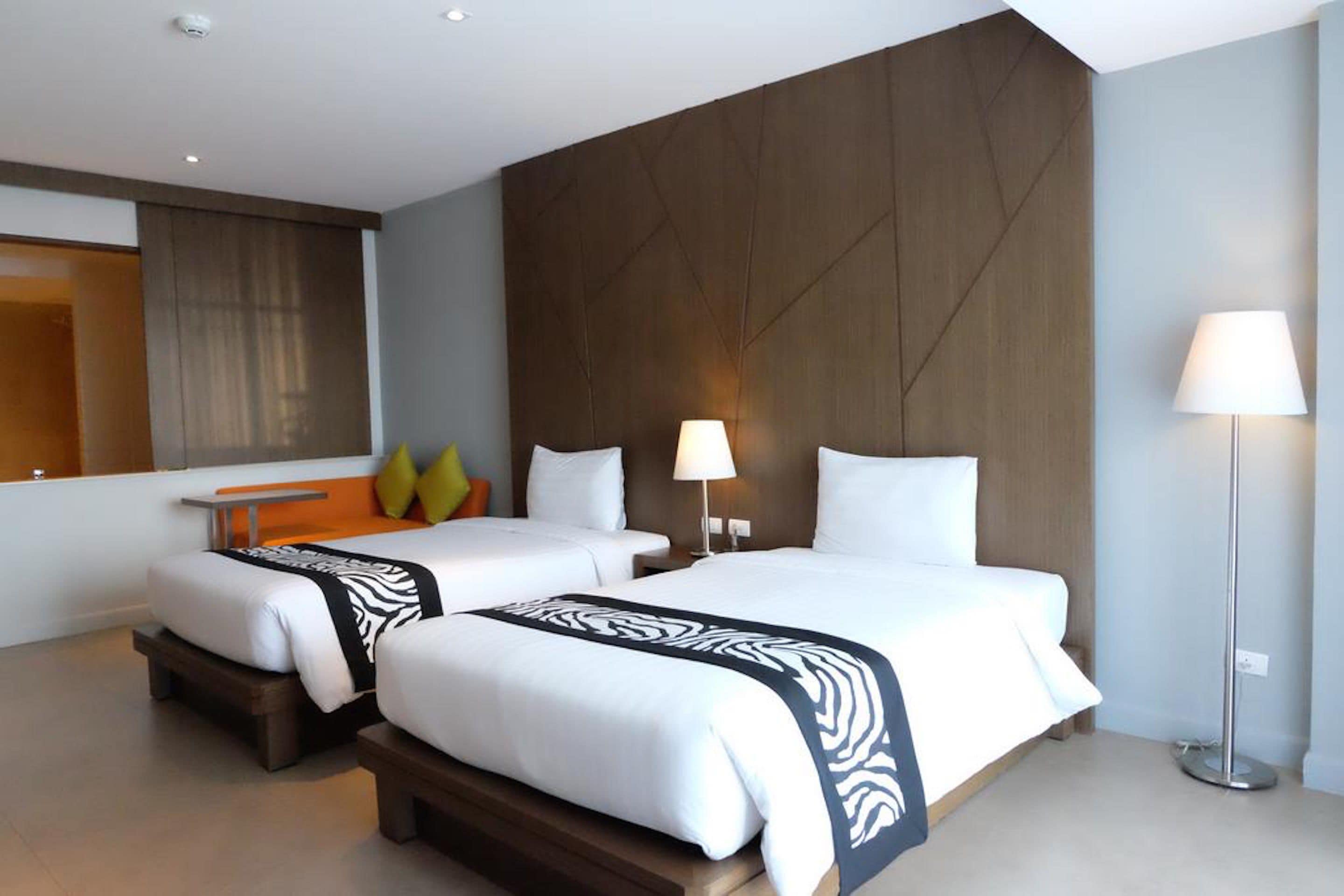 Une chambre d’hôtel avec deux lits, un grand miroir, une table de chevet et une lampe sur pied.