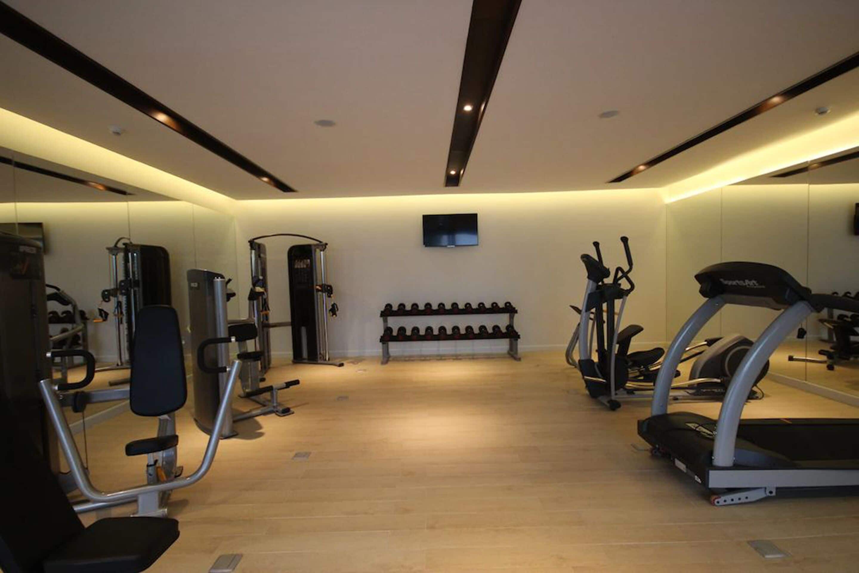 A gym with exercise equipment, a bench, and a mirrored wall.