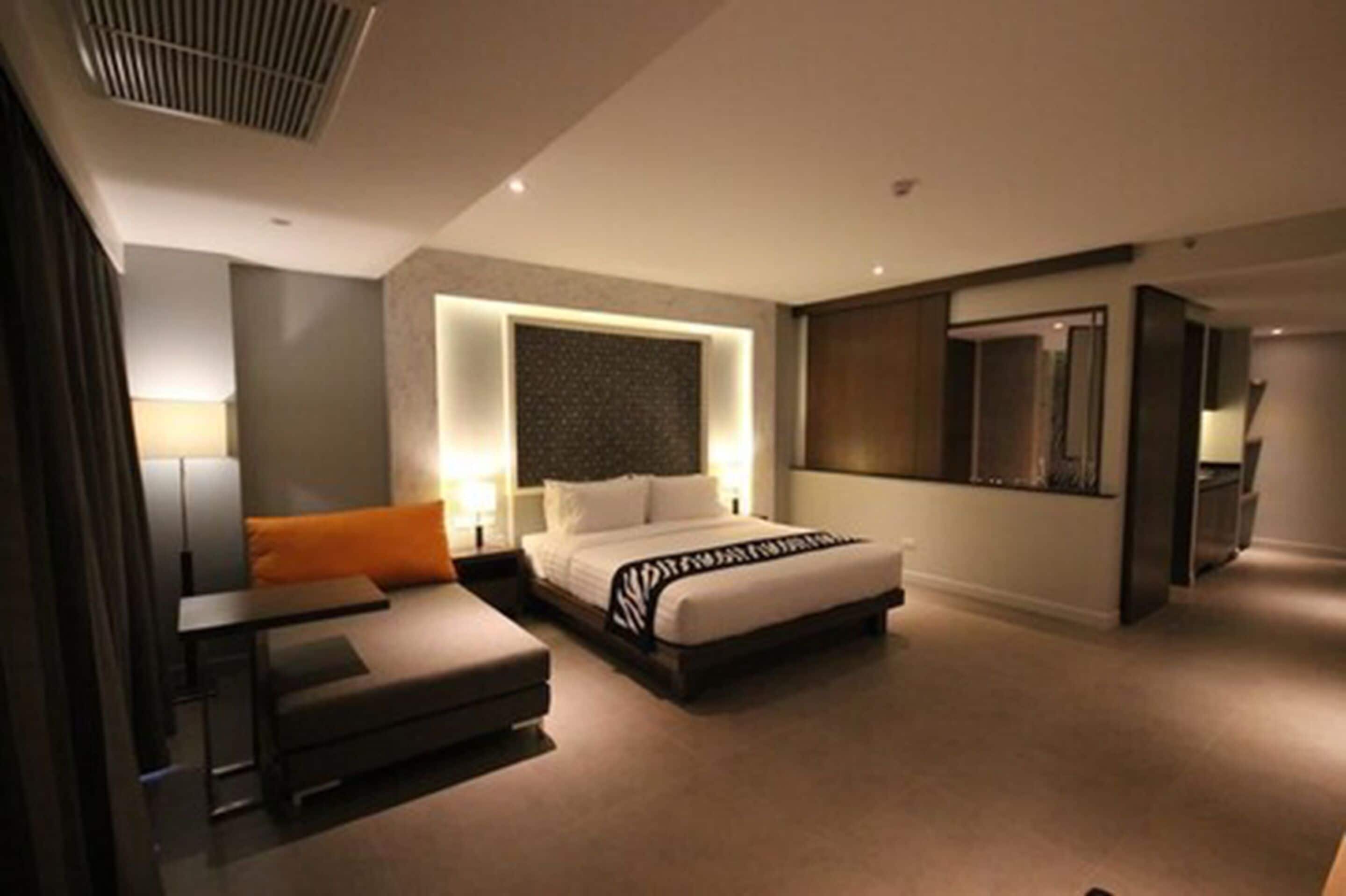A modern hotel room with a large bed, a sofa, a desk, and a TV.