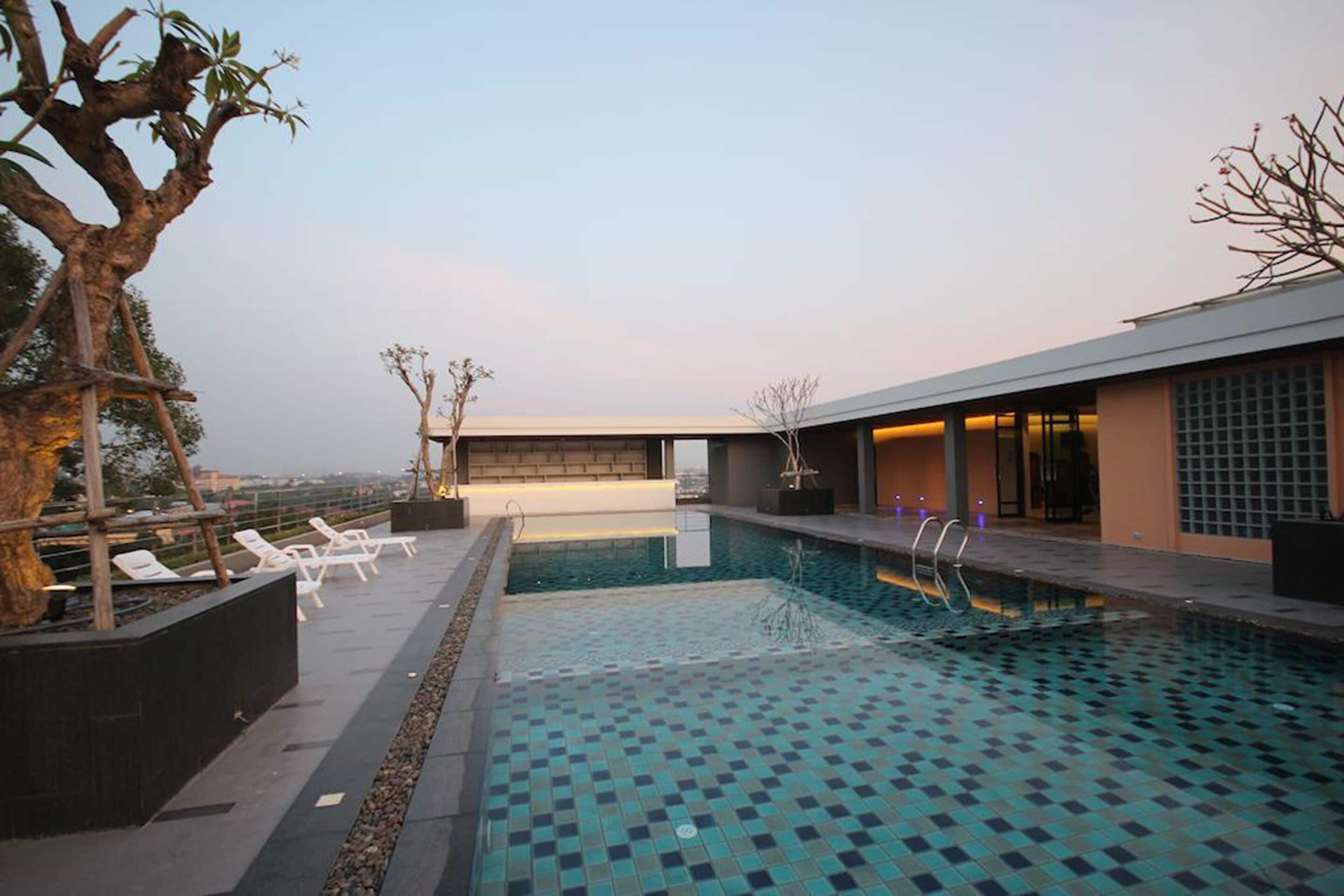 Ein Pool auf dem Dach mit Liegestühlen, ein modernes Gebäude und ein klarer Himmel.