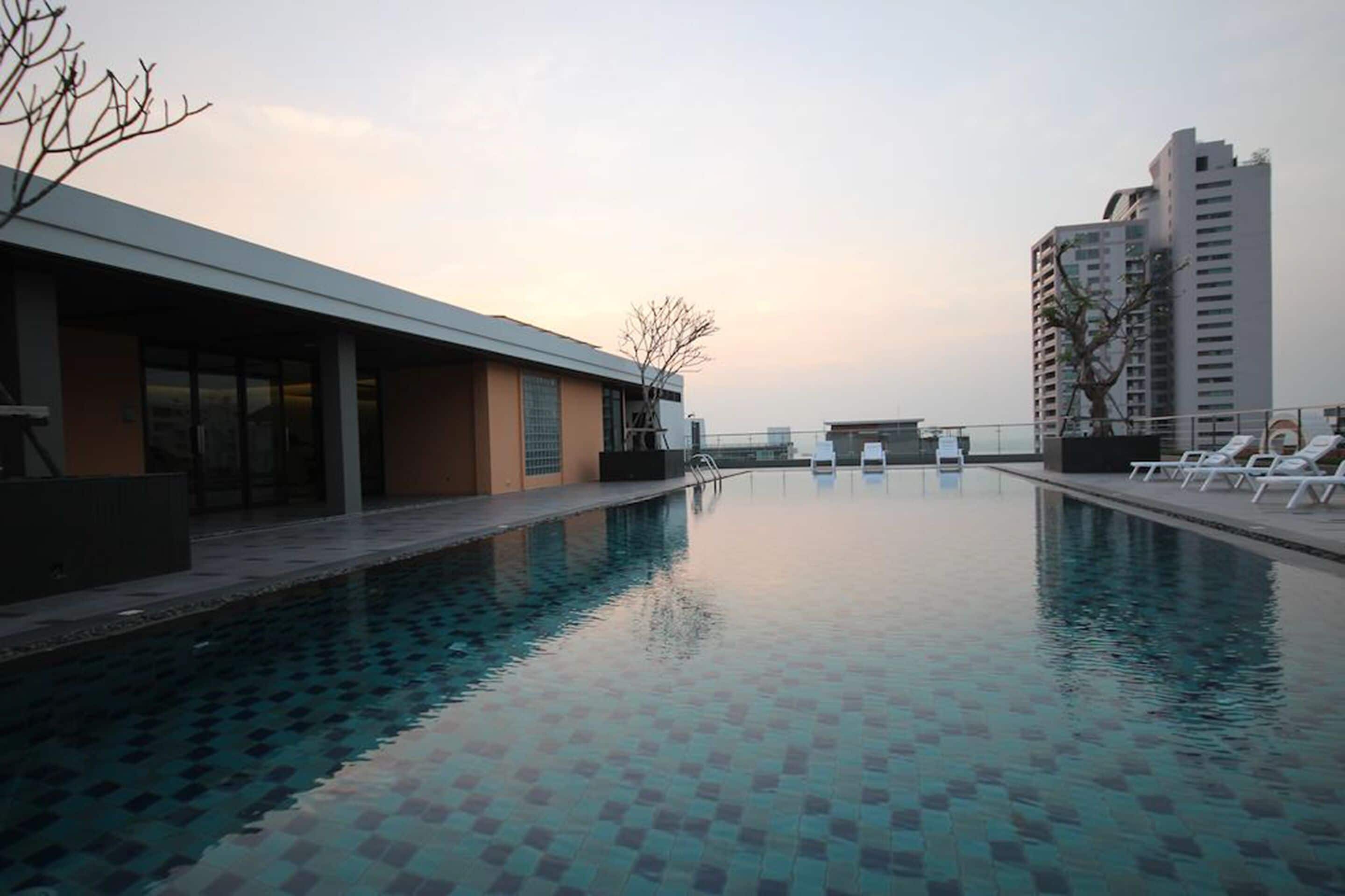 Ein Swimmingpool mit Liegestühlen, ein modernes Gebäude und ein hohes Wohngebäude im Hintergrund.