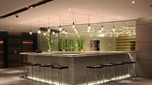 A modern bar area with a concrete counter, metal bar stools, and hanging pendant lights. - Season Five Hotel (Pattaya)