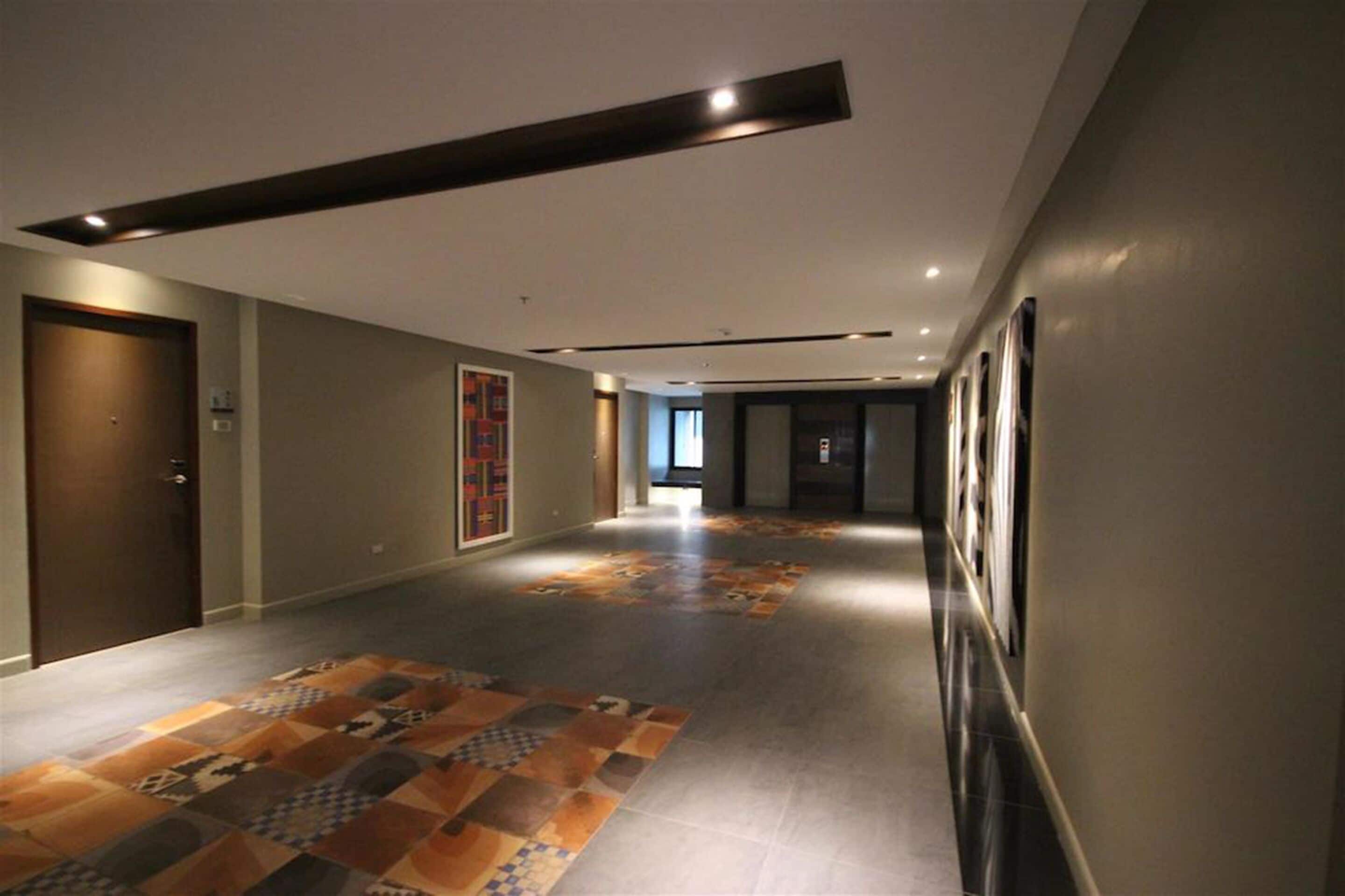 Un couloir d’hôtel moderne, avec un revêtement de sol à motifs, un éclairage encastré et des œuvres d’art encadrées accrochées aux murs.