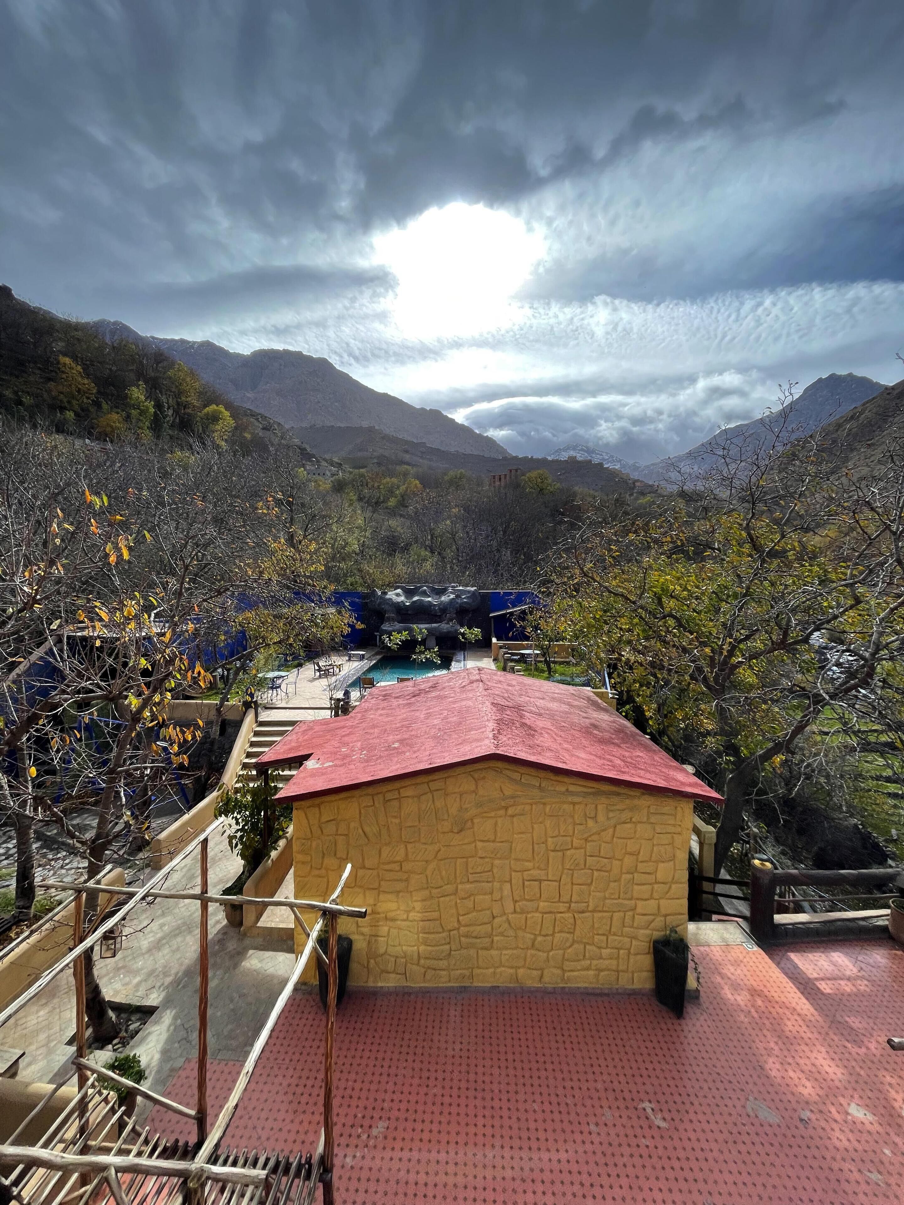 A mountain view with a building that has a red roof and stone walls.