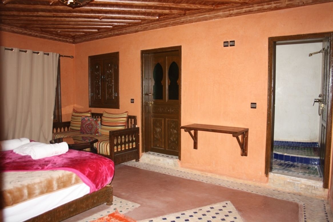 A bedroom with a bed, a wooden bench, a door, and a small table.
