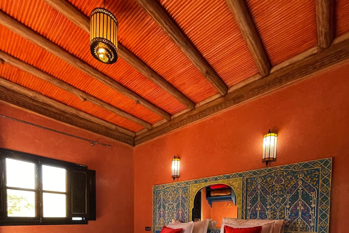 Quarto com uma cama grande, duas luminárias fixadas na parede, cabeceira estampada e janela com persianas.