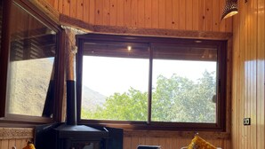 Una habitación acogedora con paredes de madera, un ventanal grande, una chimenea y dos sillones blancos.