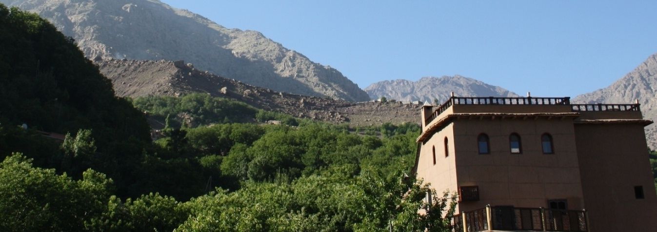 Un bâtiment doté d’un toit plat et d’un balcon, entouré de verdure et de montagnes.